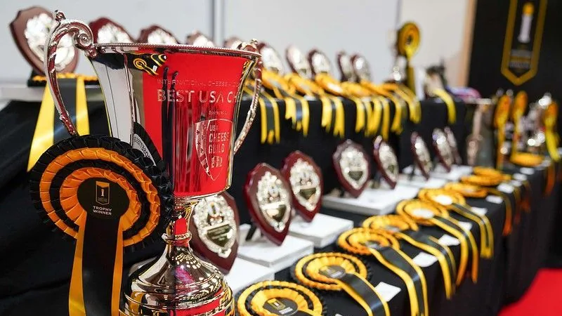 Red presentation cup and rosettes beside rows of cheese awards trophies