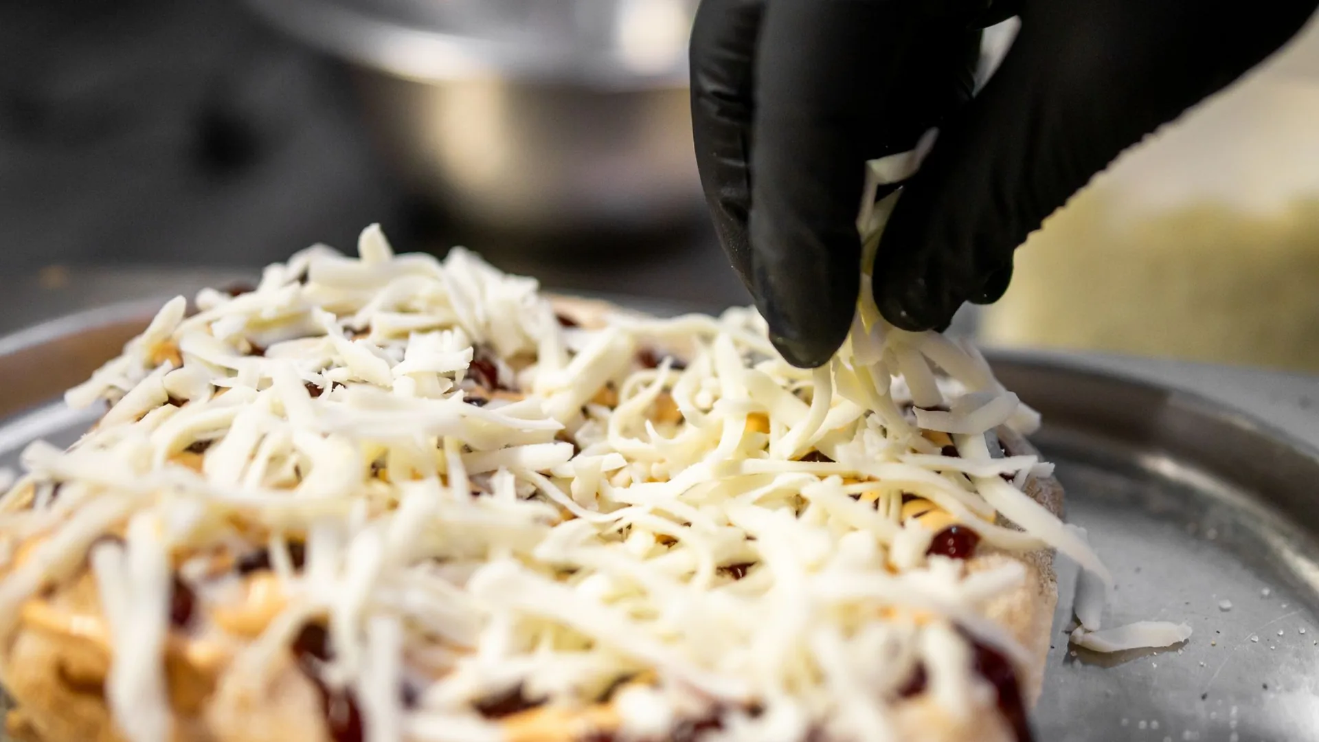 Chef in a black glove sprinkling grated cheese over a dish in a professional kitchen