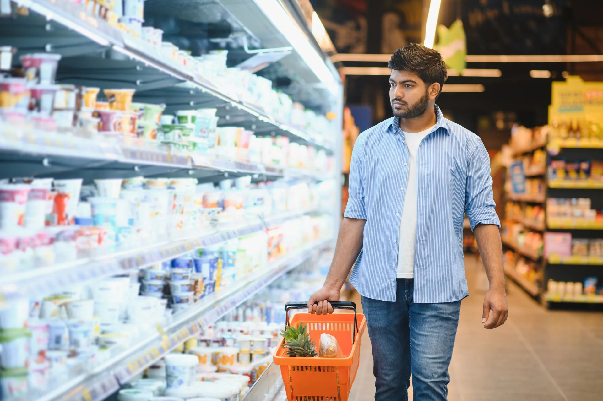 Man carrying a shopping basket past a supermarket chilled dairy aisle