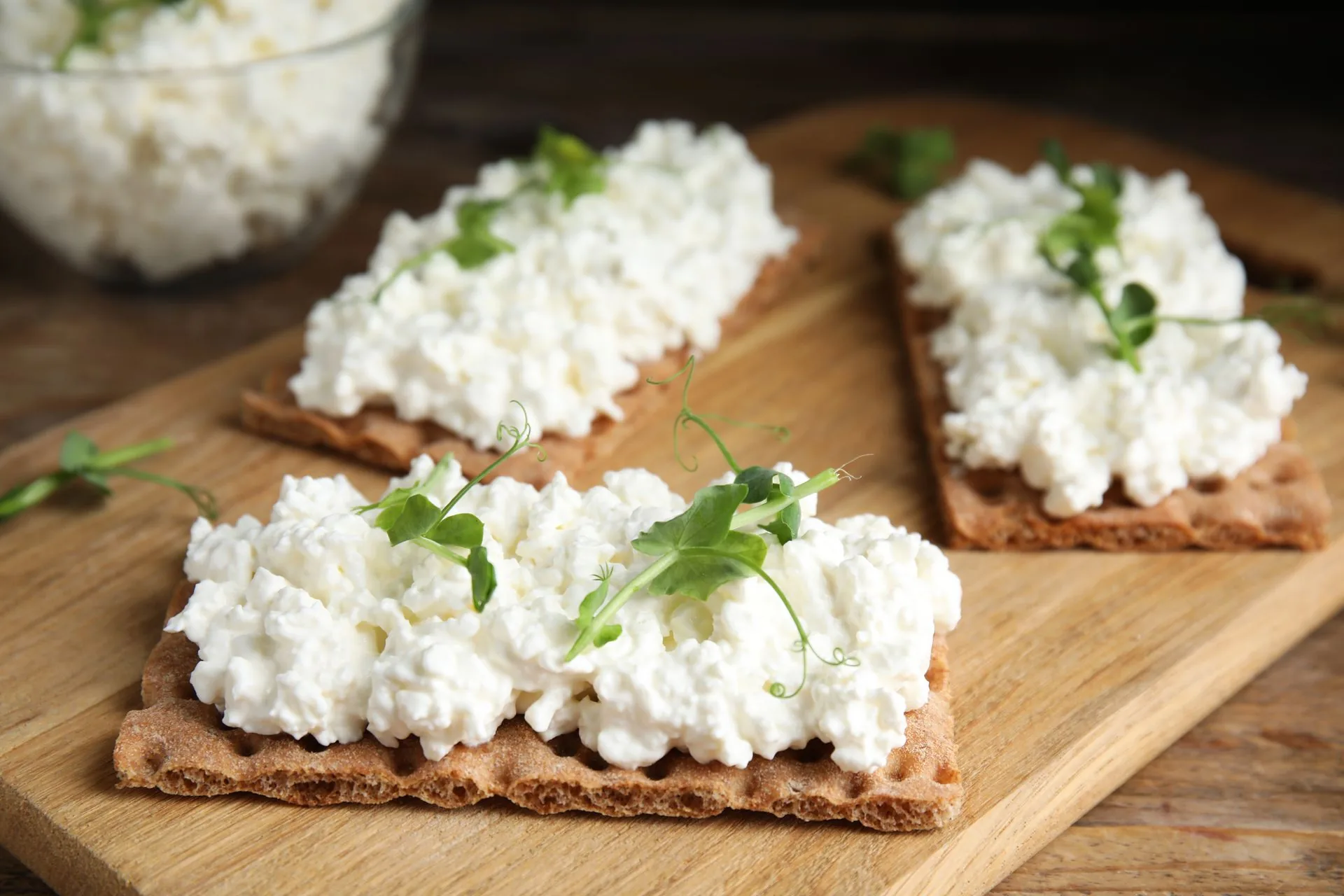 Cottage cheese piled on rye crispbread crackers topped with pea shoots on a wooden board