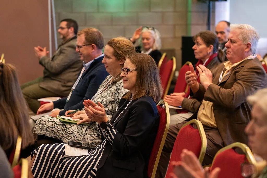 Seated conference delegates applauding on red and gold banquet chairs