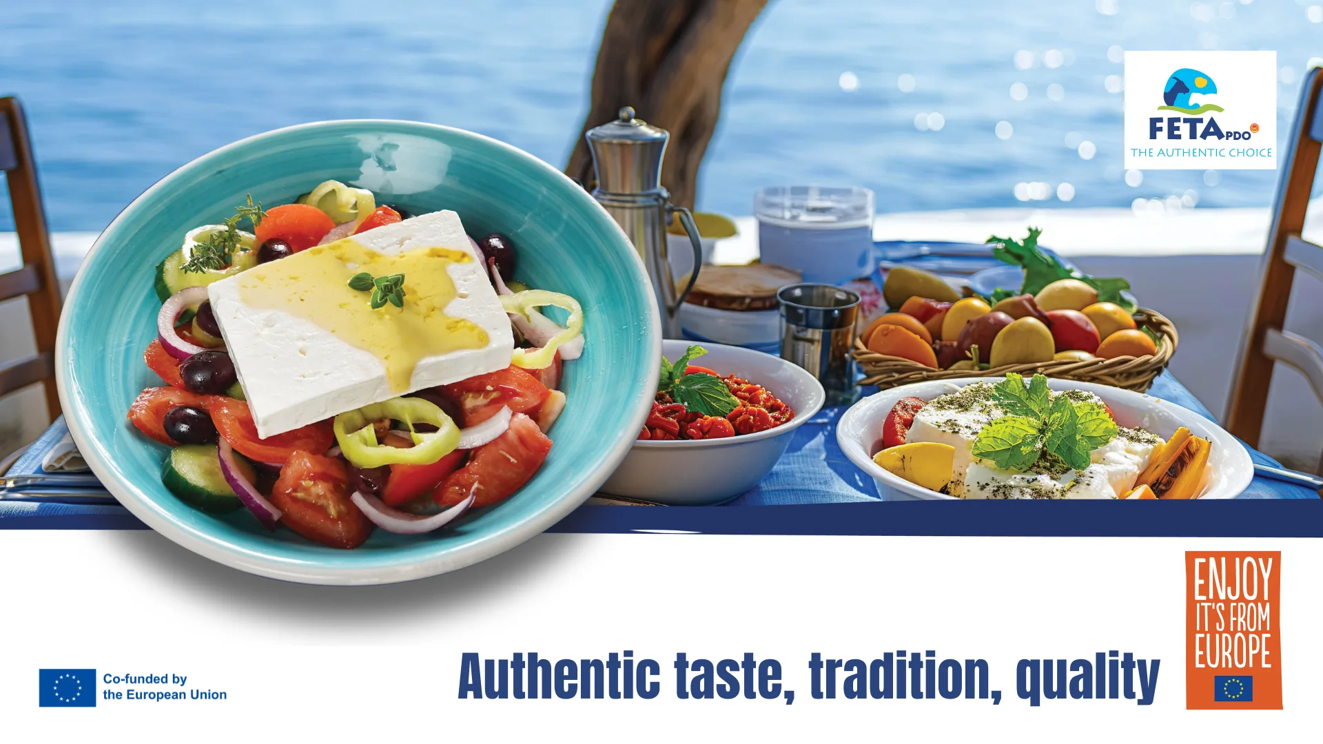 Greek salad topped with a feta block beside olives and dips on a seaside table