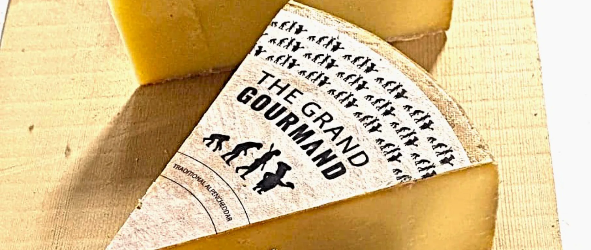 Wedge of cheese labelled The Grand Gourmand traditional Alpencheddar on a wooden board