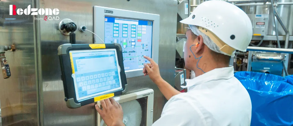Worker in hard hat operating a touchscreen control panel on a dairy line