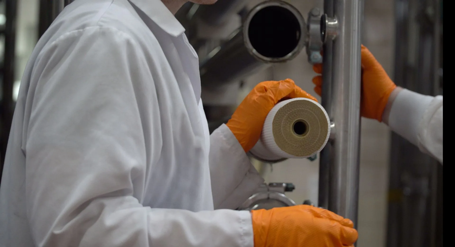 Technician in white coat and orange gloves holding a filtration membrane cartridge
