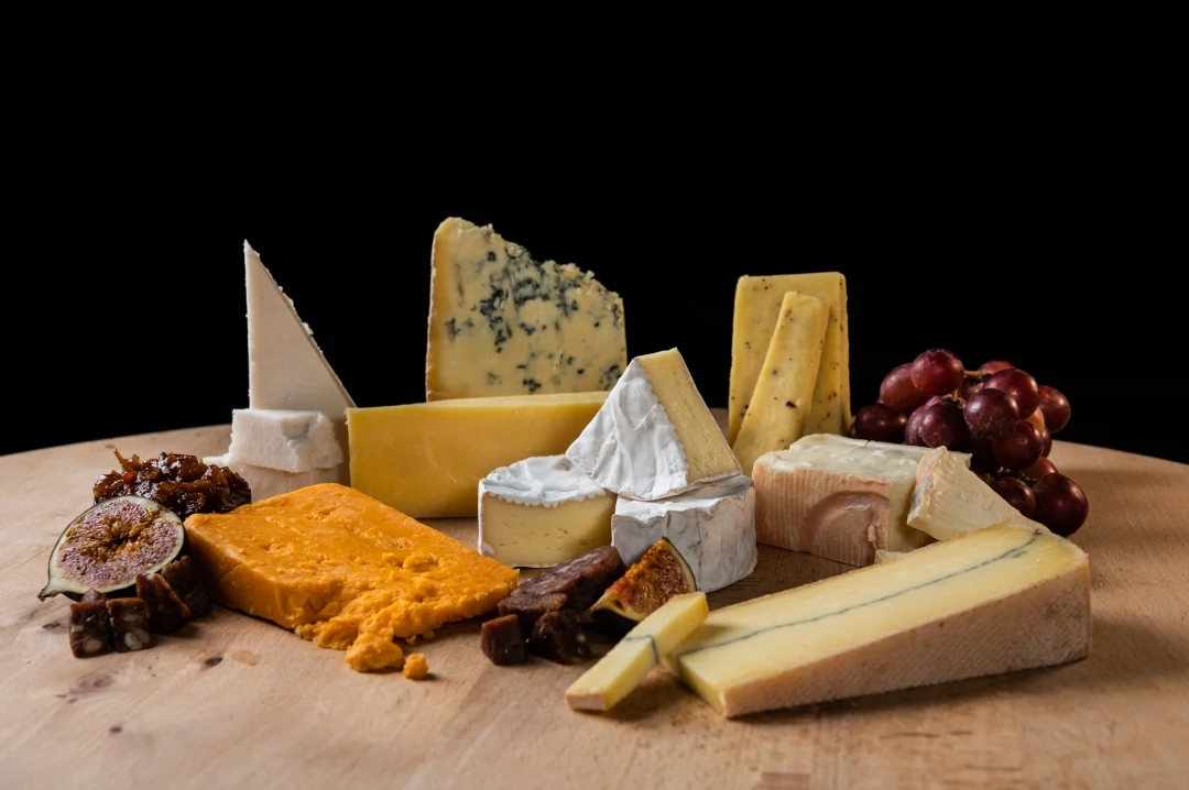 A cheeseboard of British farmhouse cheeses, including a blue, a Red Leicester and a clothbound hard cheese, with figs and grapes
