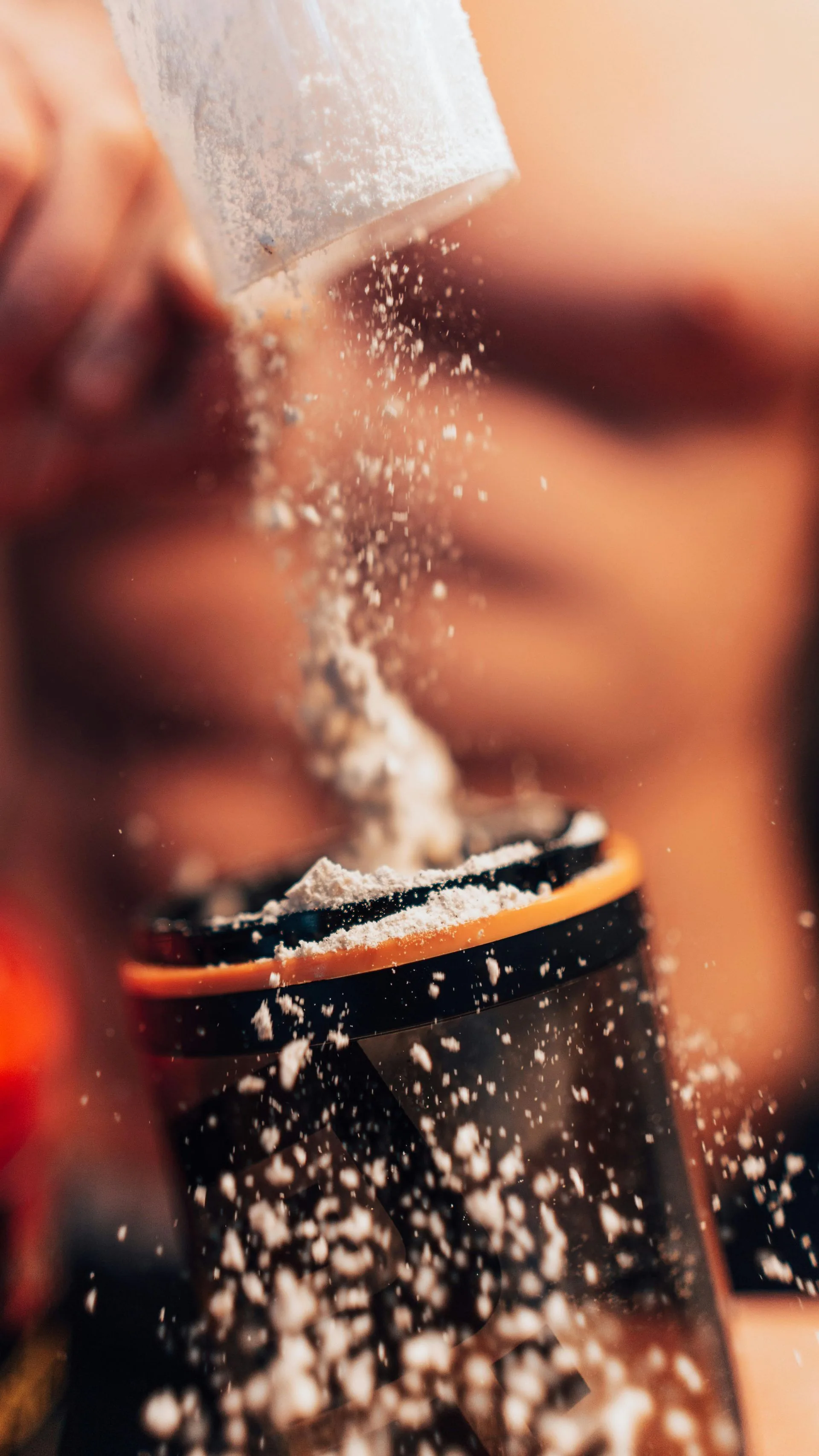 Protein powder being poured from a scoop into a shaker bottle