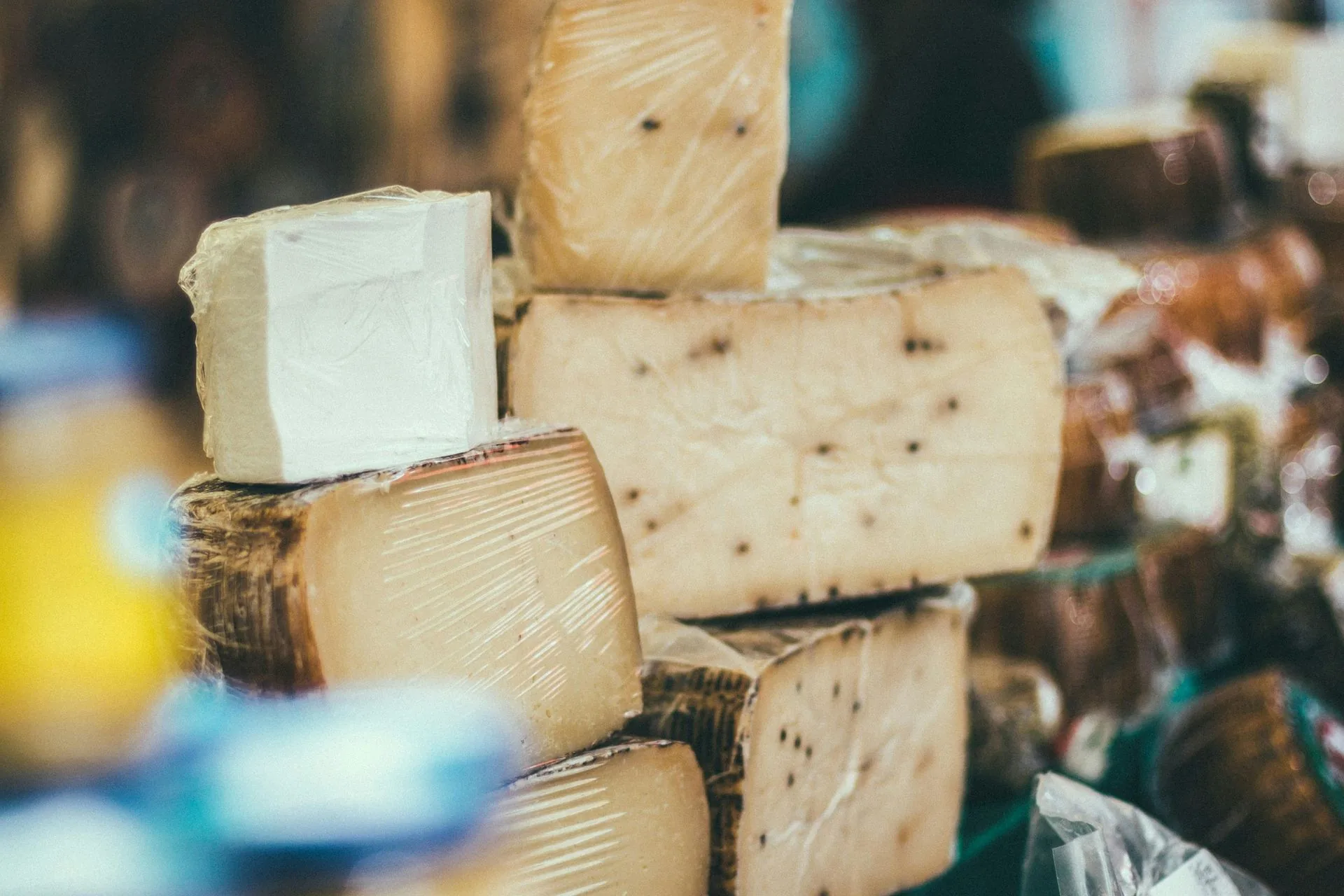 Wedges and rounds of aged cheese with dark rinds stacked on a market counter