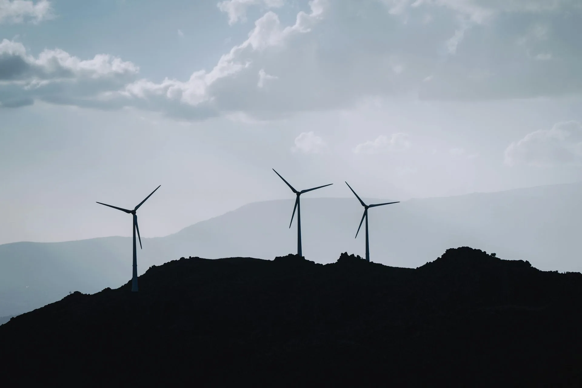 Three wind turbines silhouetted on a hilltop ridge against a cloudy sky
