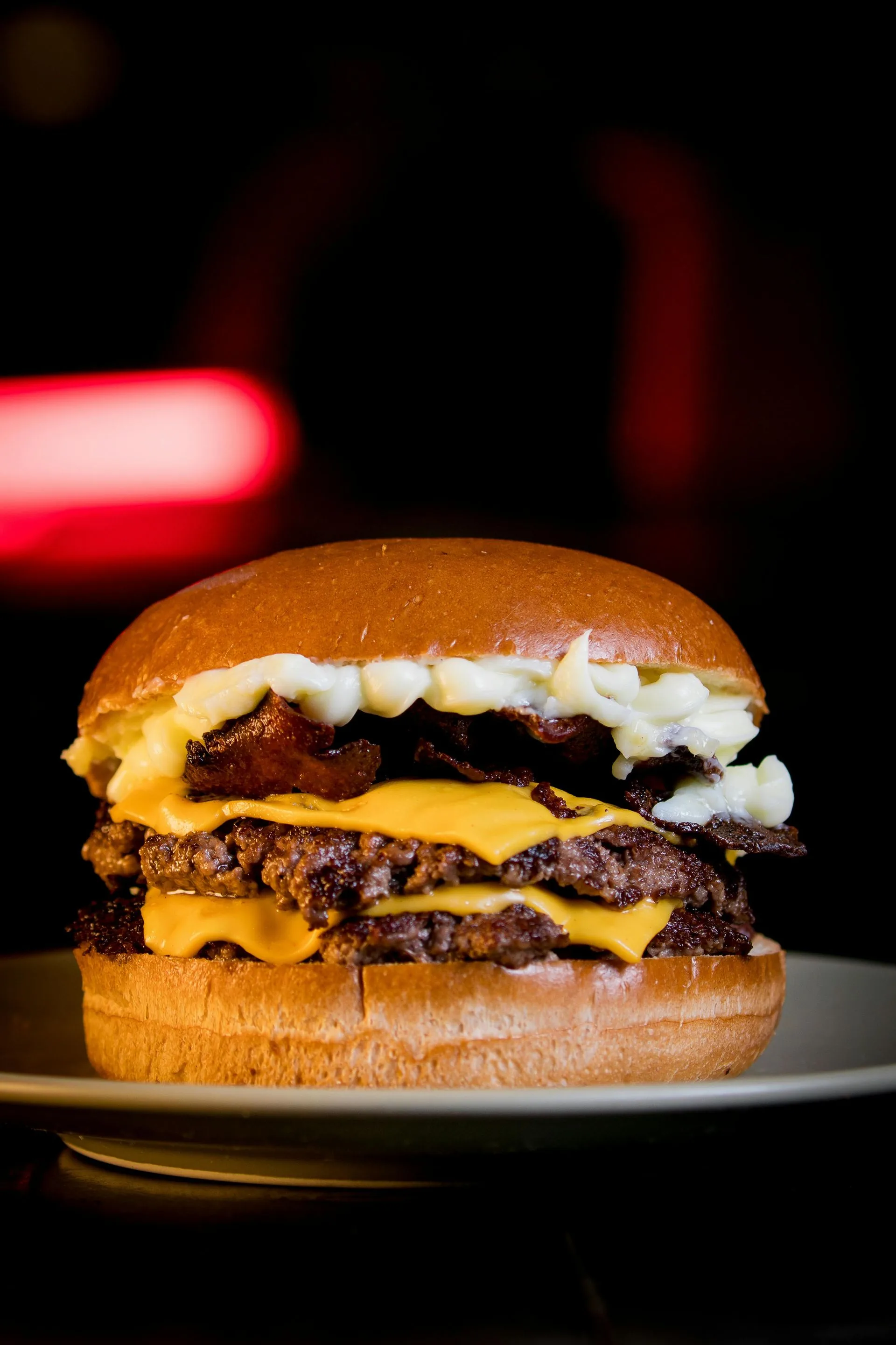 Double cheeseburger with melted cheese and bacon on a plate against a dark background