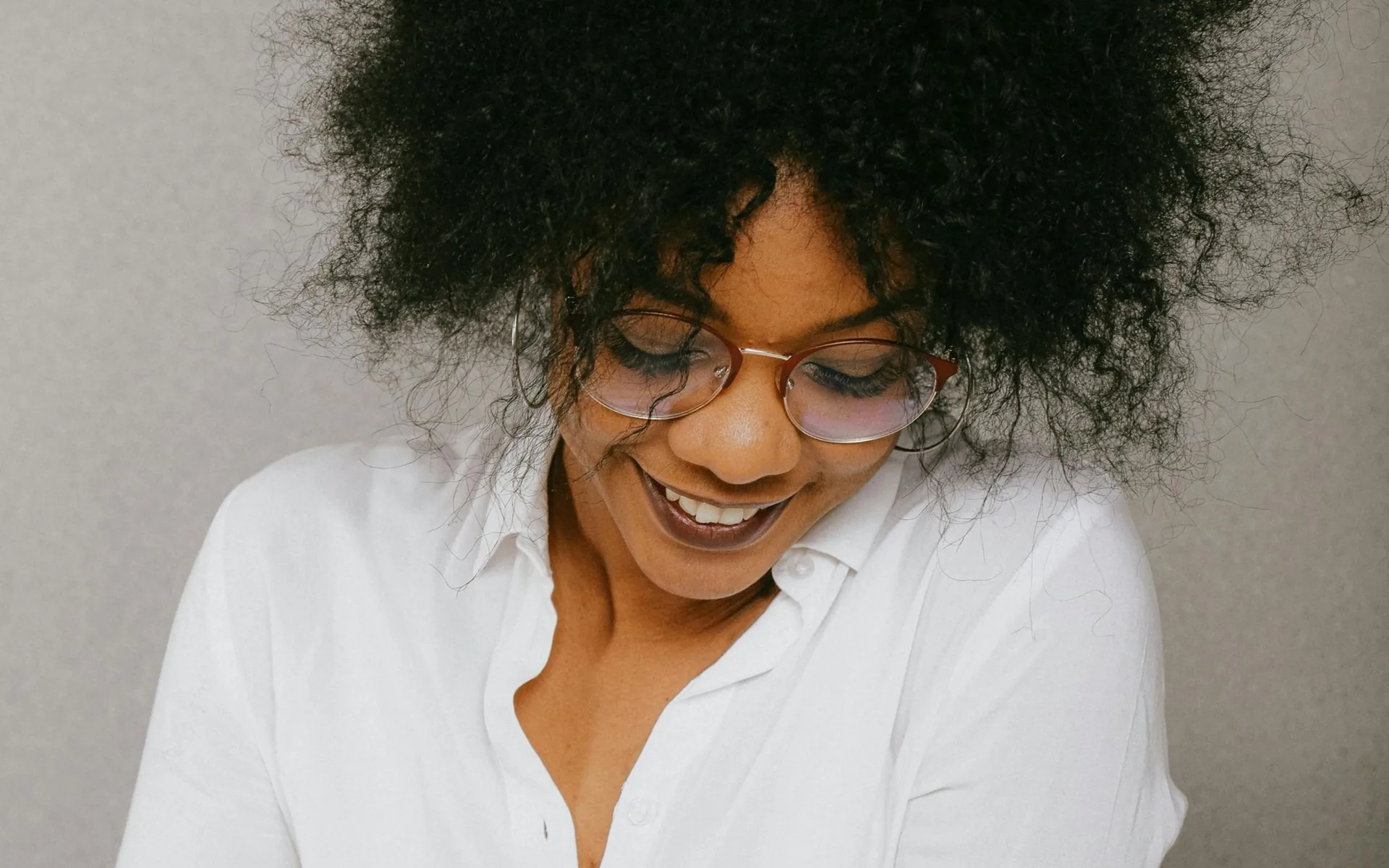 Smiling woman with curly hair and glasses in a white shirt looking down