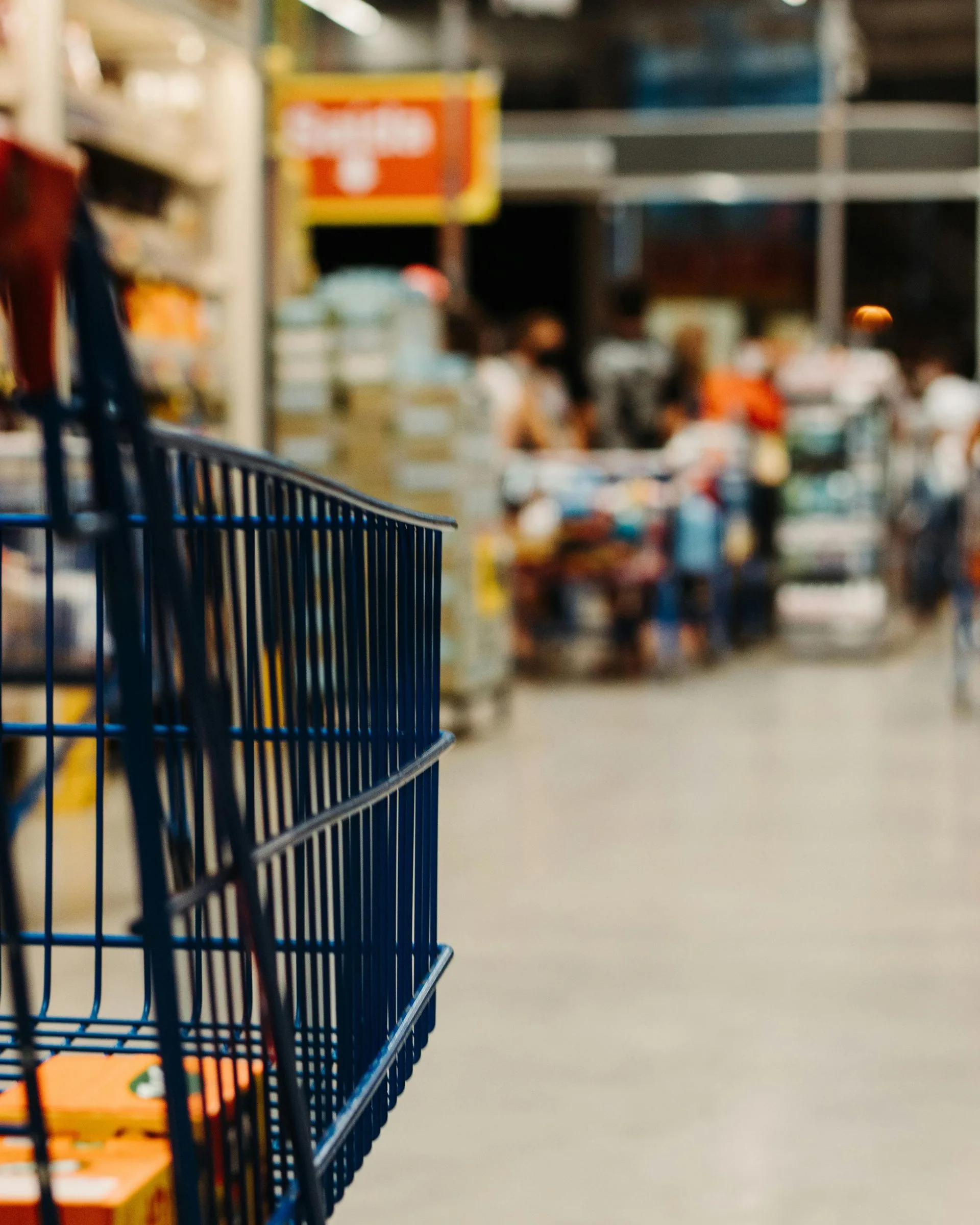 Shopping trolley in a supermarket aisle with shelves and shoppers blurred behind it
