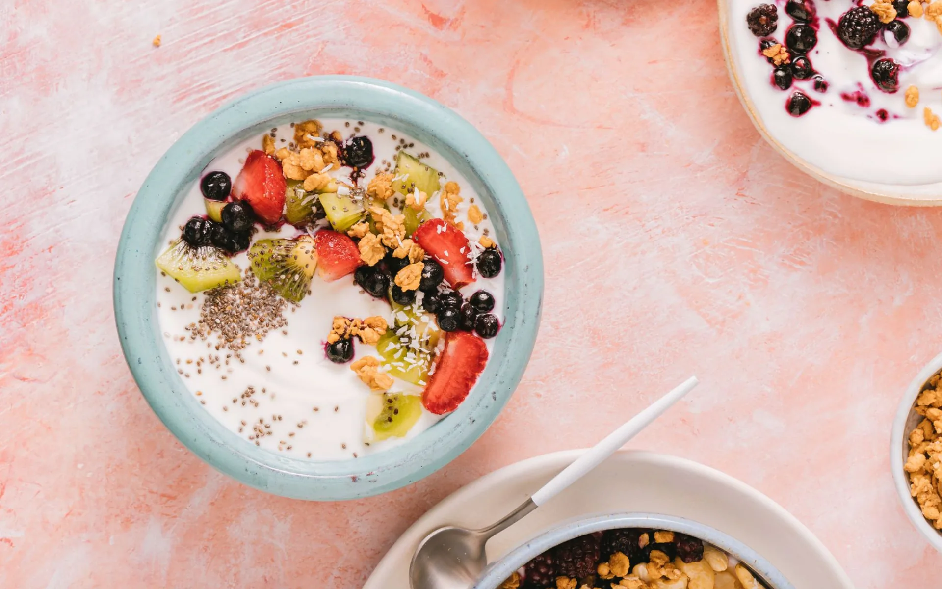 Yoghurt bowls topped with berries, kiwi, granola and chia seeds on pink