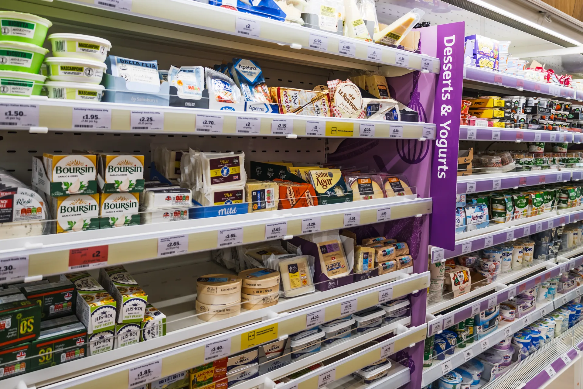A supermarket chiller of cheese, yoghurts and protein yoghurts, with shelf price labels